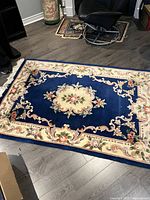Wool area rug laid flat on floor showing central medallion and floral border design in blue, cream, pink and green.