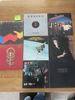 Eight vinyl album covers arranged on a wooden surface in a grid layout.