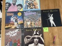 Photo showing seven vinyl records with identifiable cover art, including two Steve Martin comedy albums, movie soundtracks for Back to the Future and The Warriors, novelty Chipmunk Punk record, The Knuckleheads Curly Shuffle, and 9 to 5 soundtrack.