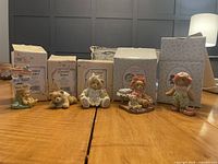 Five Cherished Teddies figurines displayed in front of their original boxes on wooden table under indoor lighting.