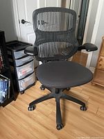 Front angled view of the black mesh office chair showing mesh backrest, padded seat, armrests and caster wheels.