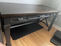 Front side of dark wood office desk showing three drawers with silver handles and sturdy legs with crossbar support