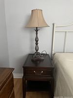 Dark wood end table supporting a decorative lamp next to bed frame
