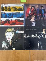 Four vinyl albums from bands The Police, Heart, Roxy Music, and Luba laid out on wood surface