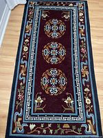 Image of a rectangular wool rug with detailed medallions and floral border patterns on hardwood floor.