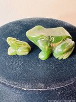 Photo of two carved jade frog figurines on a black surface, showing size and detail of each frog.