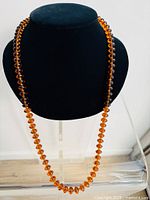 Full view of the honey coloured rounded disc glass bead necklace displayed on black bust stand