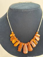 Full view of the necklace displayed on a black bust showing the arrangement of large amber beads and oval smaller amber spacers with silver-tone chain.