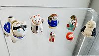 Full set of eight small Japanese figurines including various lucky cats and traditional figures displayed on clear acrylic shelf.