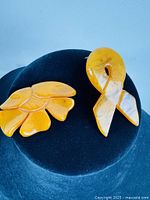 Photo showing amber-colored flower brooch and amber ribbon show pin on dark background, highlighting size and color.