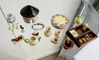 Overview of assorted miniature pottery and clay dollhouse items including hut, plates, cups, teapot, and basket with vegetables.