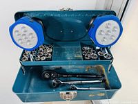 Open vintage blue metal industrial toolbox showing assorted metric and imperial sockets organized along back panel and base with two blue LED lights mounted inside lid