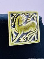Front view of the square ceramic brooch with raised horse design showing details of the glaze and embossing