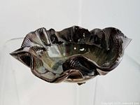 Photo of irregular abstract ceramic bowl with green and brown glaze and wavy rim, lit from front with visible signature on underside