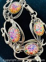 Close up photo of vintage silver-tone bracelet showing colorful glass crackle oval cabochon set in ornate metalwork link