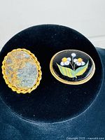 Both vintage brooches placed side by side on black velvet background showing size and design.
