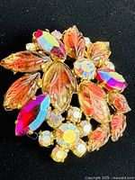 Bright close-up view of the vintage brooch showing iridescent marquise stones, detailed amber-toned glass leaves, and small faceted stones in gold-tone setting.