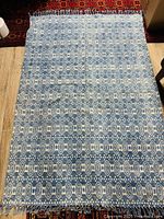 Full view of vintage blue wool woven rug laying flat on the floor, showing full blue and white geometric pattern and fringed edges.