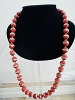 Full view of the complete vintage necklace displayed on a black bust showing the carved cinnabar beads with cloisonne inlay.