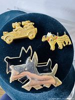 Three vintage dog brooches displayed on a black velvet bust, showing front view and details: two Westies in a car, rhinestone-embellished dog, and silver-tone dog shape.