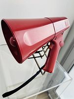 Side angle of red vintage megaphone showing funnel shape, wrist strap, and trigger handle
