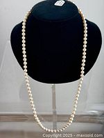 Full view of vintage knotted faux pearl necklace displayed on black mannequin bust, showing pearl strands and ornate closure at back.