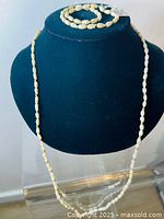 Long vintage freshwater pearl necklace displayed on black jewelry bust showing gold tone spacer beads between irregular pearls.