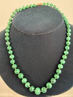 Front view of the vintage malachite round bead necklace displayed on a black bust.