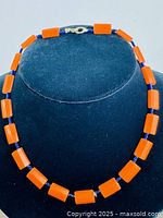 Full view of the necklace displayed on a black bust, showing the orange rectangular Lucite beads and purple bead spacers stringed together.