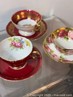 Photo of three vintage bone china tea cups and saucers placed on a clear glass surface showcasing floral designs and gold accents.