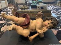 Front perspective showing full form of putto lying on its side clutching a horn