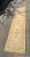 Full length view of the antique Aubusson carpet runner laid out on pavement showing its rectangular shape and floral decorative pattern in beige tones.