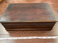 Top view of closed rectangular rosewood box showing smooth polished wood surface with visible wear and scratches. Measuring tape indicates dimensions around 18 inches long.