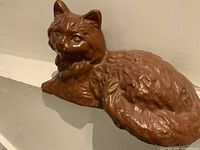 Image showing brown ceramic or concrete cat doorstop resting on a white surface against a neutral wall, highlighting the detailed sculpted fur and facial features