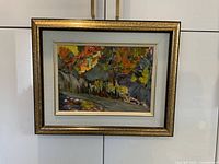 Framed watercolour landscape painting showing autumnal trees and pathway, hung on a white wall.