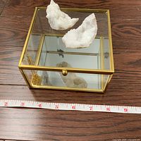 Glass and brass framed trinket box placed on a wooden surface with two large white quartz geode sections inside. Measuring tape shows about 9 inches width.