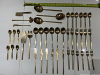 Full layout of vintage goldtone cutlery pieces showing the full 44-piece set including forks, spoons, and serving utensils with a measuring tape for reference.