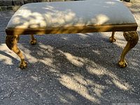 Front view of gilt bench showing rectangular upholstered seat and carved cabriole legs with ball-and-claw feet