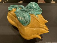 Front angle view of vintage Italian covered dish shaped like a yellow fruit or vegetable with textured turquoise leaves on top as lid.