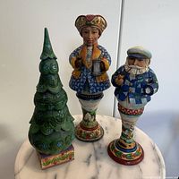 Three Jim Shore Heartwood Village figurines on a marble base - green Christmas tree, tall nutcracker holding lantern, smaller nutcracker with pipe missing a hand