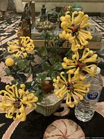Front view of the vintage glass chrysanthemum plant showing six yellow flowers, green leaves, and ceramic pot next to a water bottle for scale.