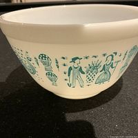 Side view of the white glass bowl showing the green Amish Butterprint design of figures and farm motifs around the exterior.