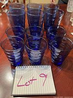 Photo showing all 12 blue drinking glasses, 6 large at the back and 6 smaller at the front, set on a table.