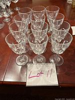 Twelve clear vintage Arcoroc wine goblets arranged on a wooden table, showing all items in the set.