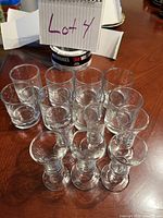 14 assorted clear glass shot glasses of three different styles arranged on a wooden surface