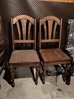 Two solid wood dining chairs showing curved backrests and turned legs