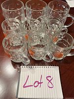 Nine clear glass beer steins arranged in two rows, three large and six small, showing textured geometric block patterns and handles.