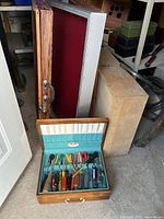Three display cases leaning against a wall: two wood and glass with latches, one with red felt interior, plus one wood box in front containing various screwdrivers.
