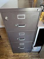 Front view of three-drawer metal filing cabinet with top drawer lock and handles
