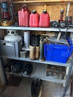 Metal shelving stocked with red fuel containers, boots, propane tank, ropes, compressors, and hand tools